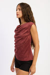 Woman wearing a maroon sleeveless top with a draped design on a white background