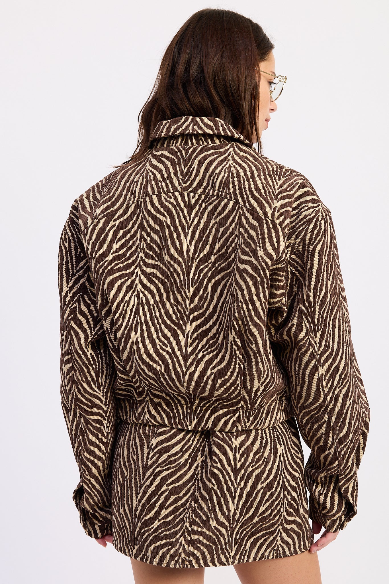 A woman shown from the back wearing a brown and beige zebra-print jacket with a matching tie belt, set against a plain white background.