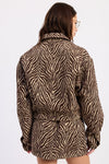 A woman shown from the back wearing a brown and beige zebra-print jacket with a matching tie belt, set against a plain white background.