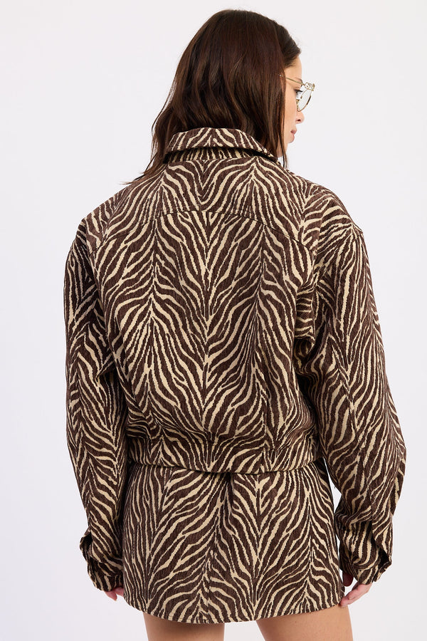 A woman shown from the back wearing a brown and beige zebra-print jacket with a matching tie belt, set against a plain white background.