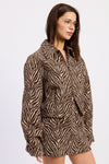 A woman wearing a brown and beige zebra-print jacket, shown from a side profile against a plain light gray background.
