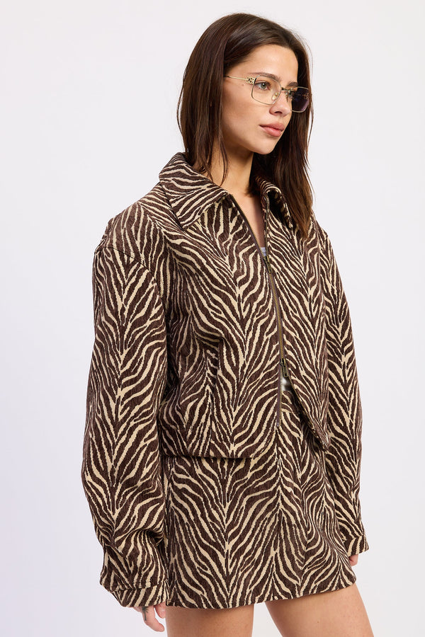 A woman wearing a brown and beige zebra-print jacket, shown from a side profile against a plain light gray background.