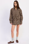 A model wearing a brown and beige zebra-print shirt jacket, styled with gray socks and brown leather loafers against a plain white studio background.