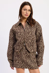 A woman wearing a brown and beige zebra-print jacket with a front zipper, photographed against a plain light gray studio background.
