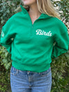 Model wearing a kelly green zip up with birds written in cursive on left chest area