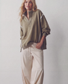 A woman modeling an oversized olive green half-zip pullover with white contrast panels and light beige drawstring pants against a plain light gray studio background.