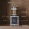 A premium soy candle in a plaid-patterned glass jar sits on top of its matching box against a dark brown background. White text around the product highlights features such as premium fragrance oils, 100% cotton wick, gluten free and phthalate free ingredients, made in USA, and 50+ hour burn time.