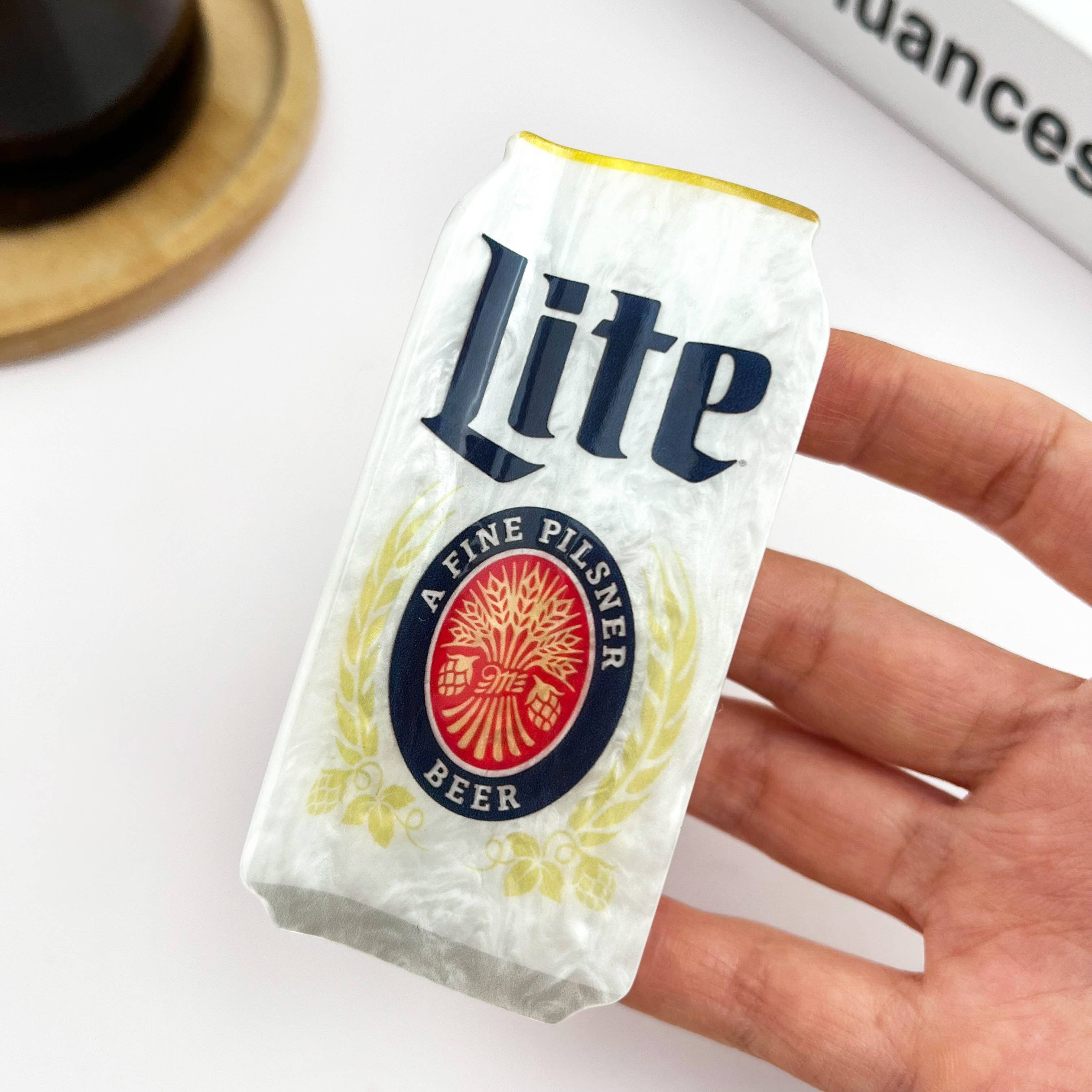 Hand holding a Miller Lite beer can claw clip against a white background