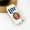 Miller Lite beer can clip on a white surface with a wooden coaster in the background