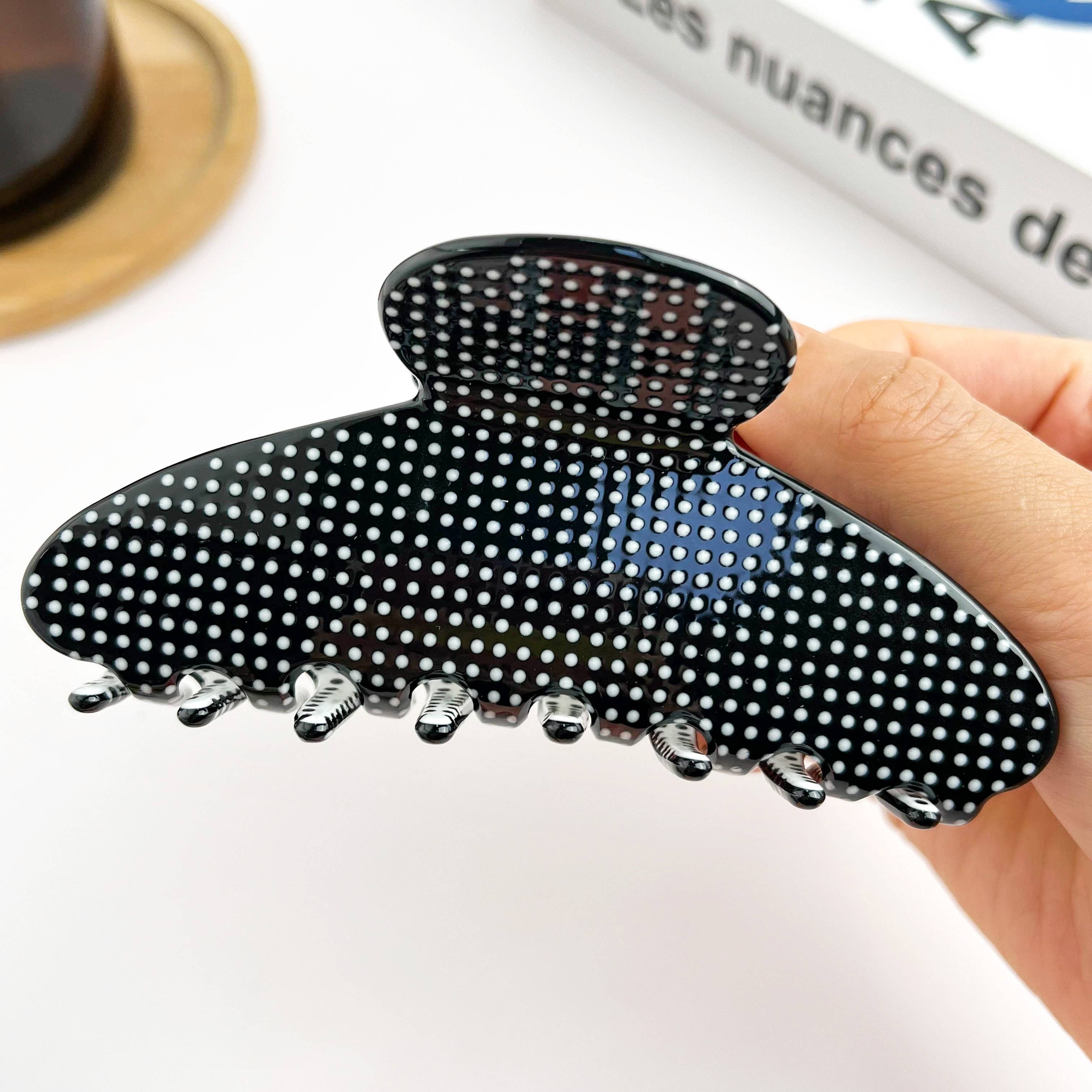 Black hair clip with white polka dots held by a hand on a light background