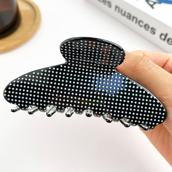 Black hair clip with white polka dots held by a hand on a light background