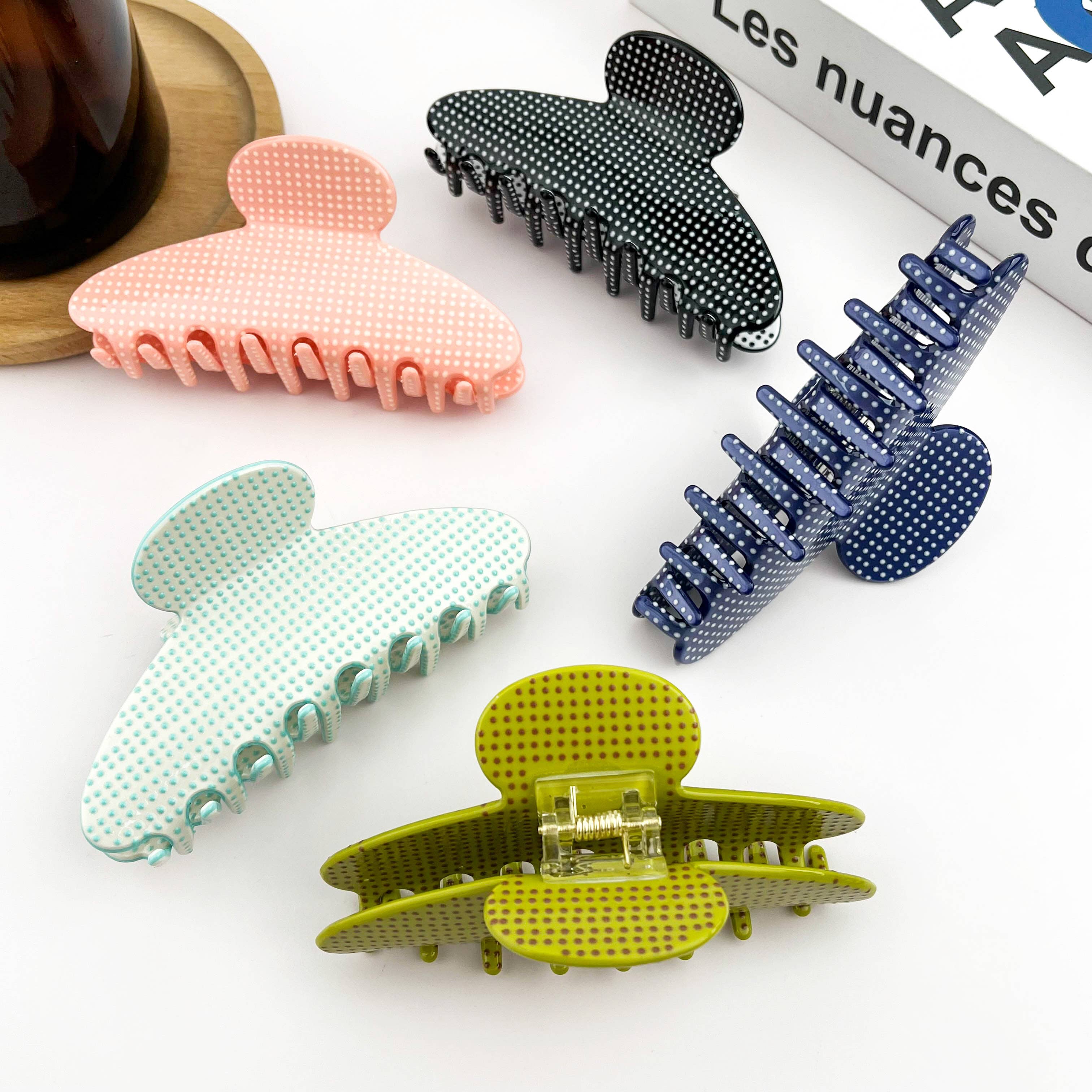Five colorful hair clips on a white surface with a magazine in the background.