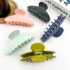 Five colorful hair clips on a white surface with a magazine in the background.