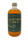 A bottle of Wood Stove Kitchen Pumpkin Spice Coffee & Cocktail Syrup, featuring an amber-colored liquid in a clear glass bottle with a dark green label and gold lettering.