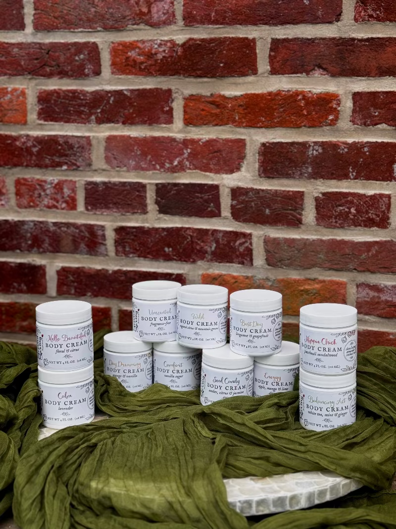 Jars of body cream stacked against a brick wall with green fabric.