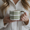 Person holding a mug with a green plaid pattern