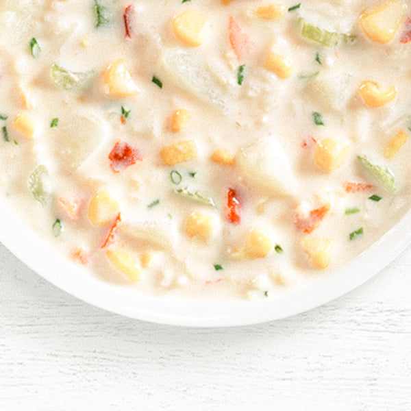 A bowl of Illinois Prairie Corn Chowder with visible pieces of corn, red pepper, and herbs in a creamy broth.