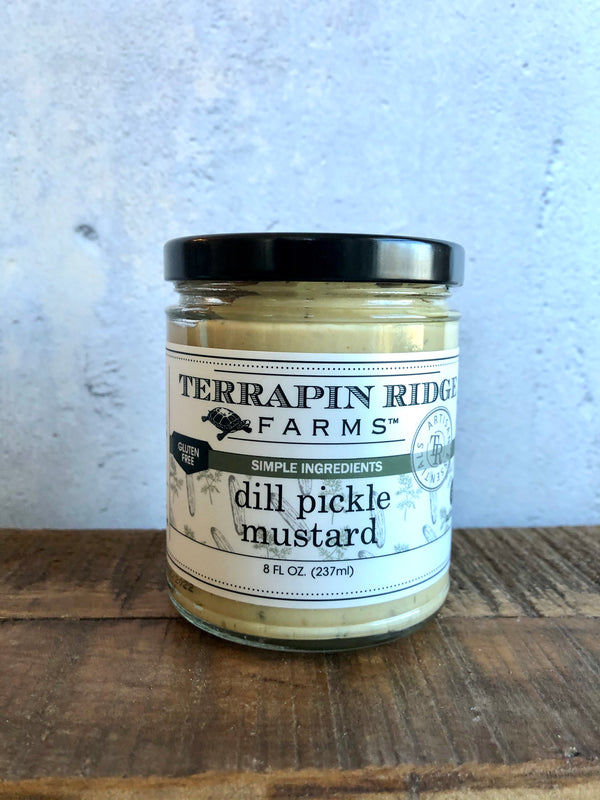 A jar of Terrapin Ridge Farms Dill Pickle Mustard on a wooden surface with a label that includes the product name and a brief description.